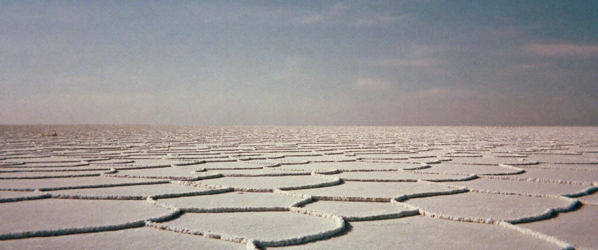 A cracked white salt flat stretching to a low horizon under a bleached sky.