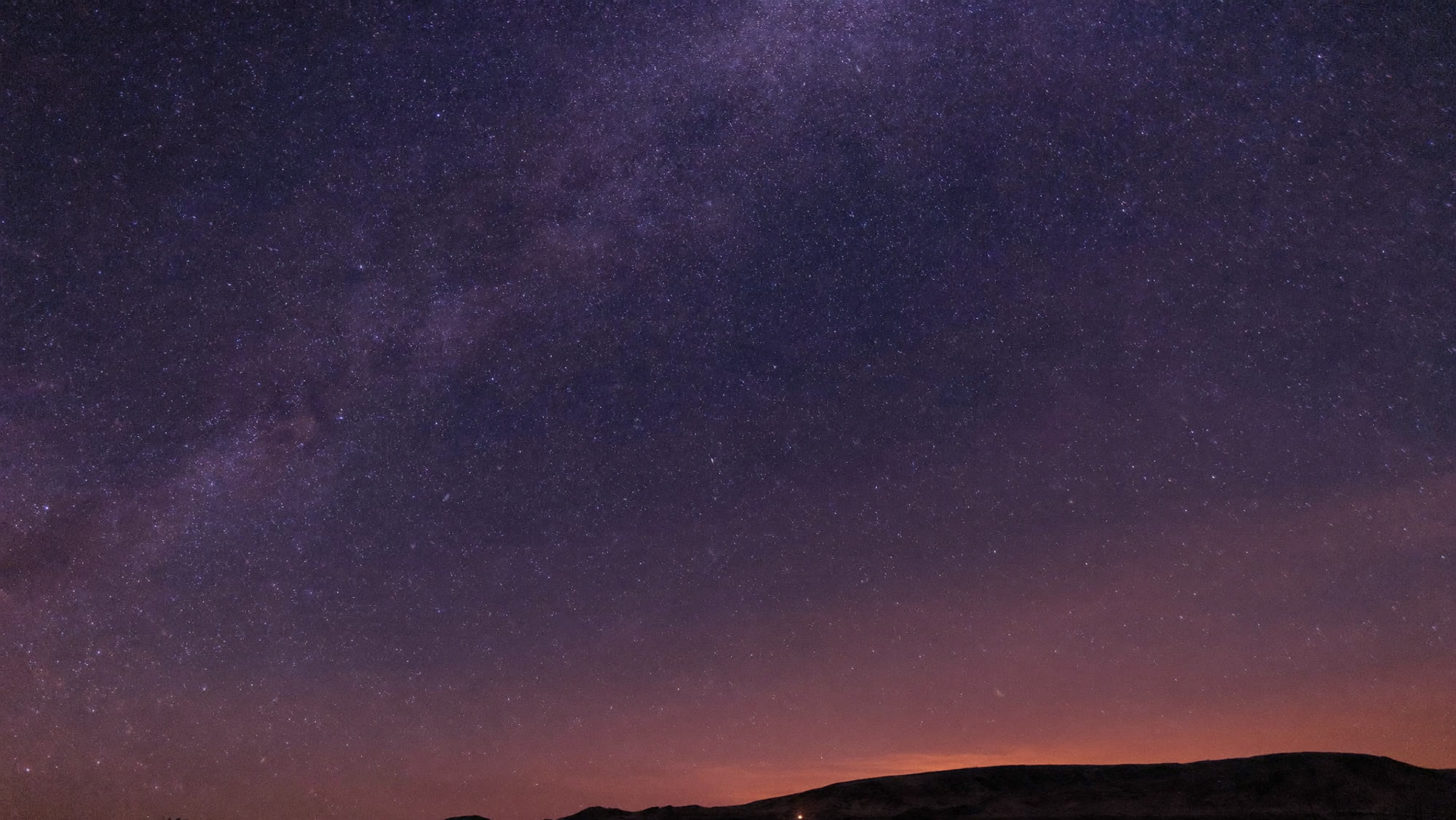 The Milky Way arching over a dark high-desert plain in a long exposure, stars dense from horizon to zenith.
