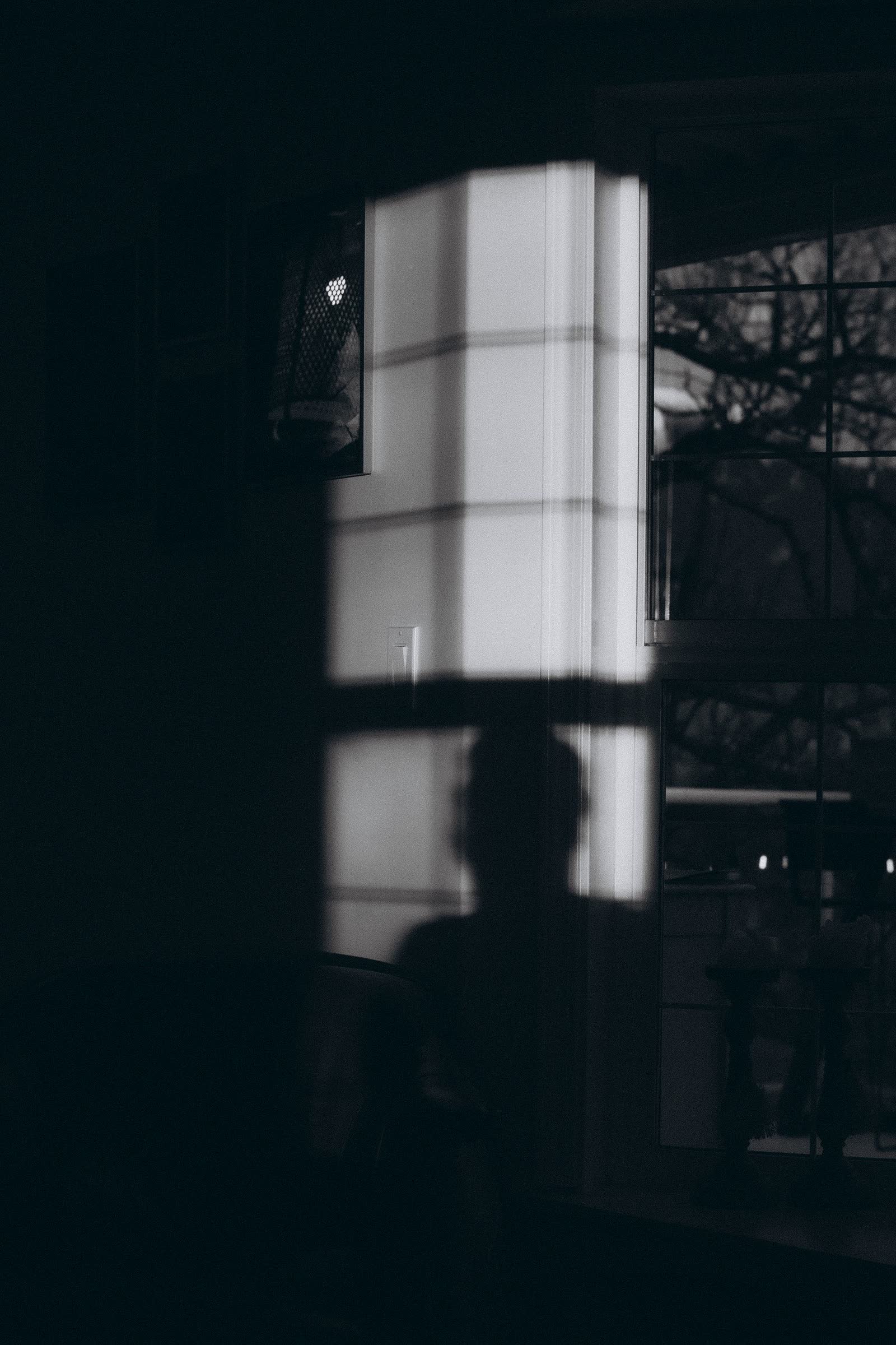 Figure silhouetted against a window in a dark interior